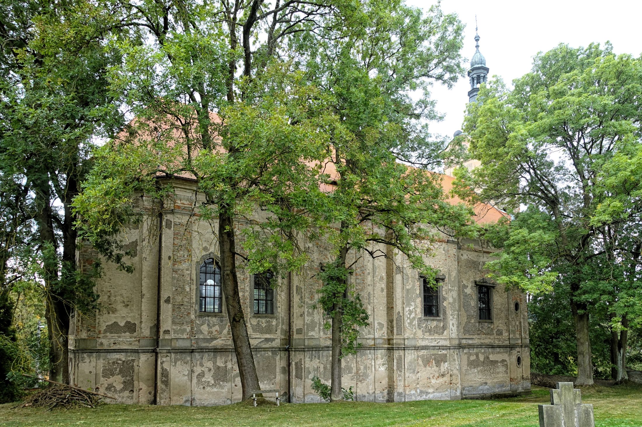 Kostel částečně zakrytý letními stromy.